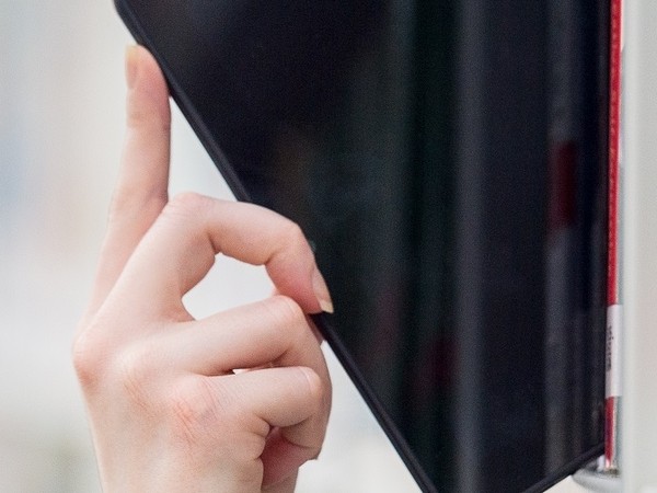 Close-up of a hand pulling a black tablet from a shelf or kiosk with a white background