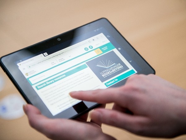 Person using a tablet device displaying a library website with text and a logo that reads 'ILLRVARHAGOR BOOKS & BEYOND'