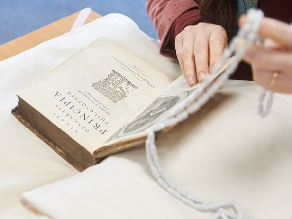 Hands turning the page of an old book titled 'Dissertations Principia Philosophiae' placed on a white cloth on a table.