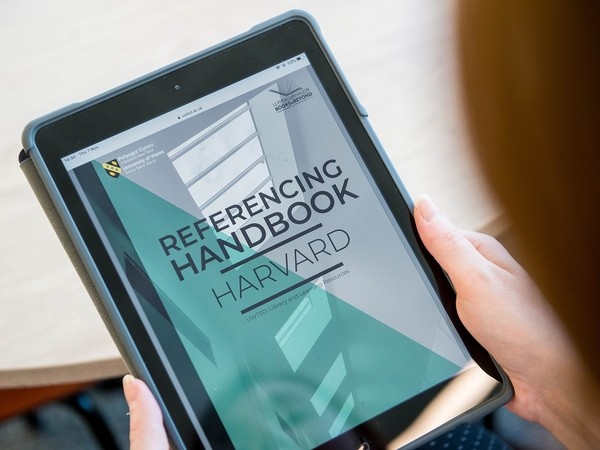 Person holding a tablet displaying a digital copy of the "Referencing Handbook Harvard" from the University of Queensland Library