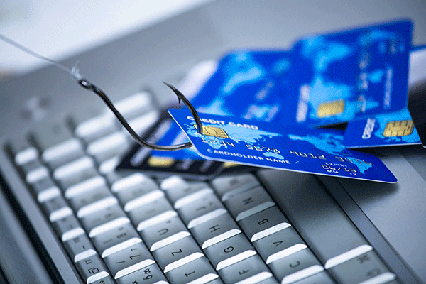 Fishing hooks hooked into credit cards placed on a computer keyboard, symbolizing online credit card fraud or phishing scams.