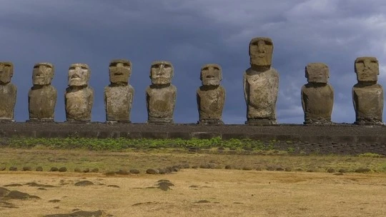 Row of nine large stone Moai statues on a platform against a cloudy sky on Easter Island.