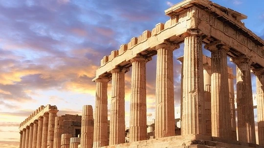Ancient Greek temple ruins with tall stone columns under a colorful sunset sky with scattered clouds.