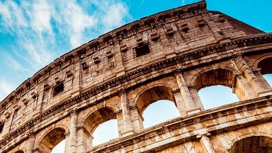 Close-up view of the ancient Roman Colosseum's stone arches and upper structure under a partly cloudy blue sky