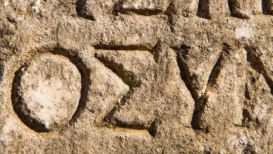 Close-up of ancient stone engraving showing carved Greek letters on a rough textured surface.