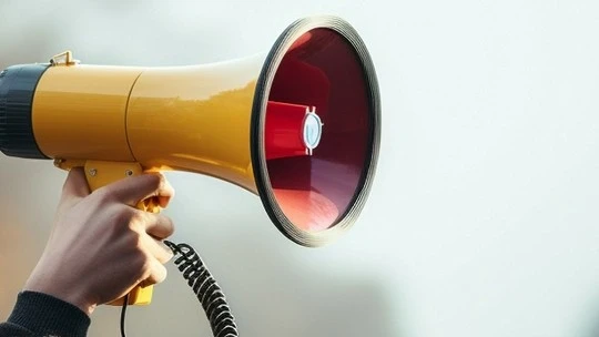 Close-up of a hand holding a yellow megaphone against a light gray background