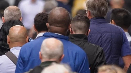 Rear view of a diverse crowd of people walking closely together in an indoor setting.