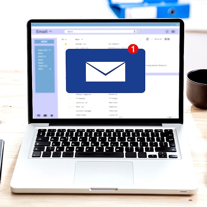 Laptop on a wooden desk with an email inbox open on the screen, showing a large blue envelope icon with a red notification badge indicating one unread email, a cup is placed to the right of the laptop.