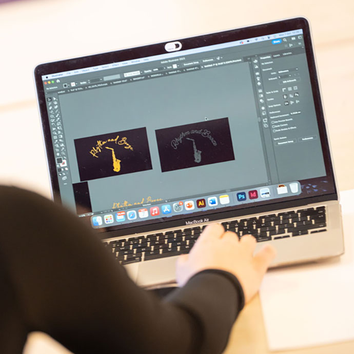 Person working on a MacBook Air laptop using Adobe Illustrator, editing two logo designs featuring a saxophone and the text 'Rhythm and Brass' on a black background.