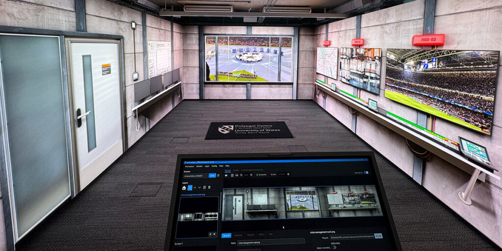 Control room with multiple large monitors displaying sports events and a computer screen showing surveillance footage and settings.