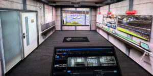 Control room with multiple large monitors displaying sports events and a computer screen showing surveillance footage and settings.